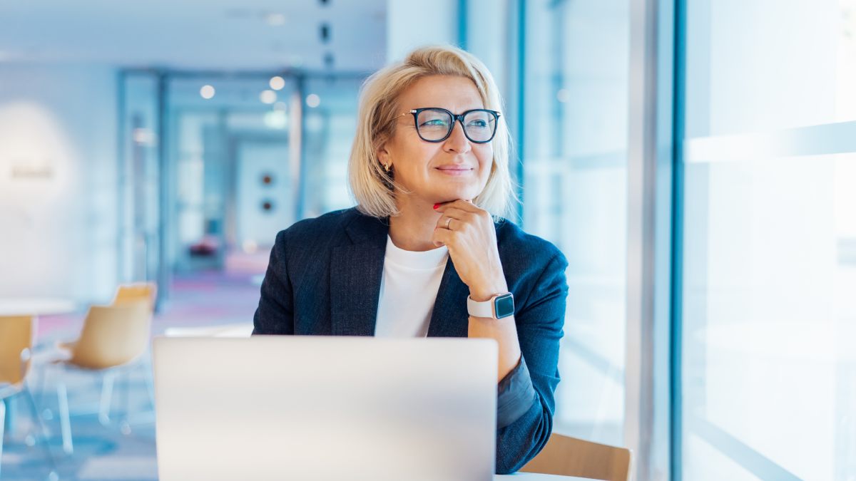 Femme qui a une cinquantaine d'année, pensive, devant son ordinateur.