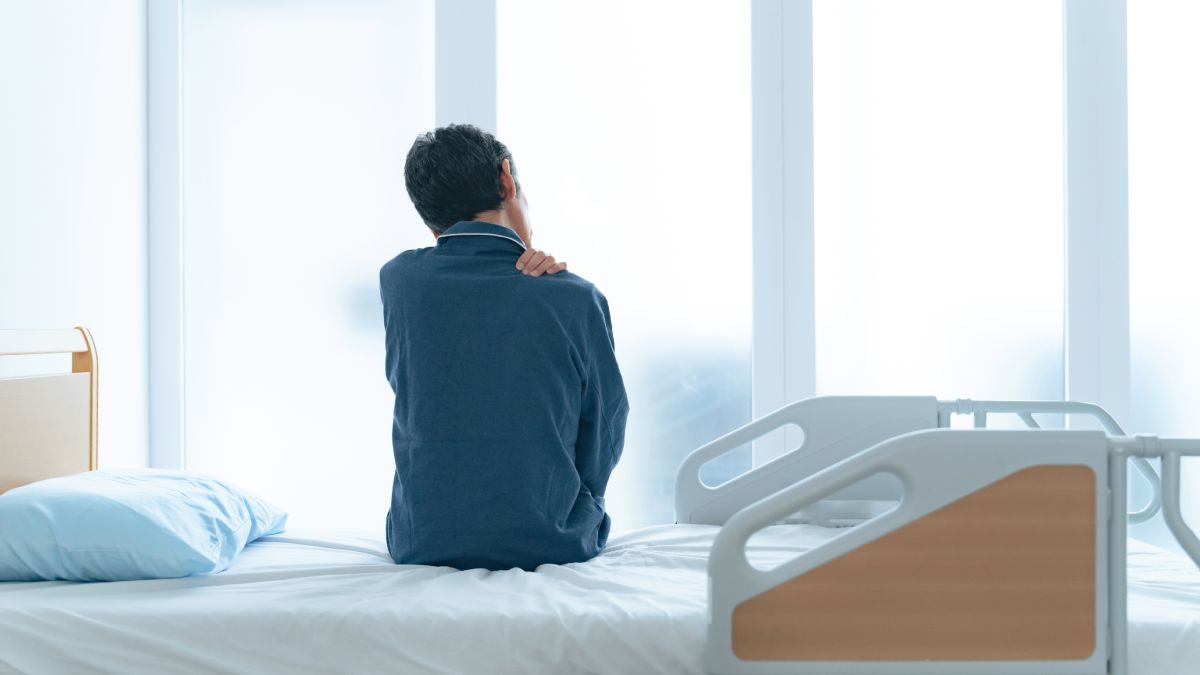 Homme seul dans sa chambre d'hôpital se tenant l'épaule.