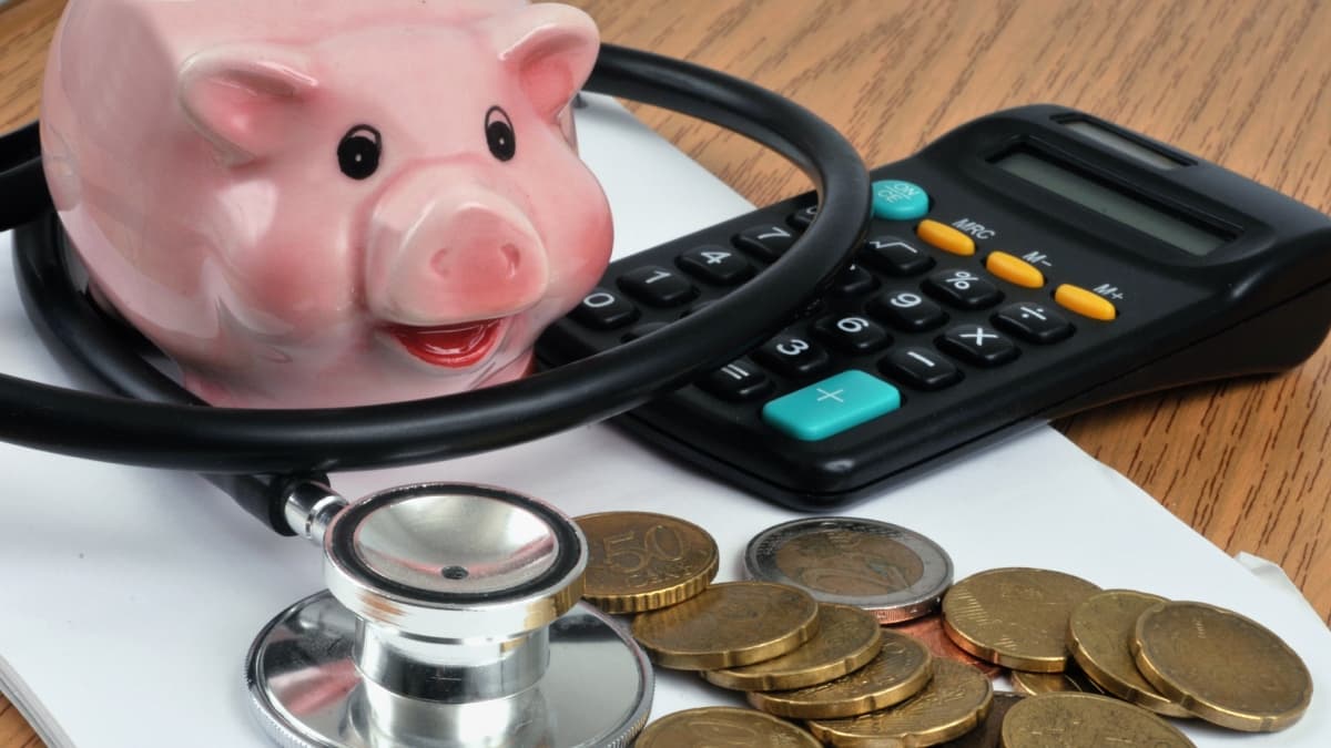 Tirelire, pièces de monnaies, calculatrice et un stéthoscope sur une table.