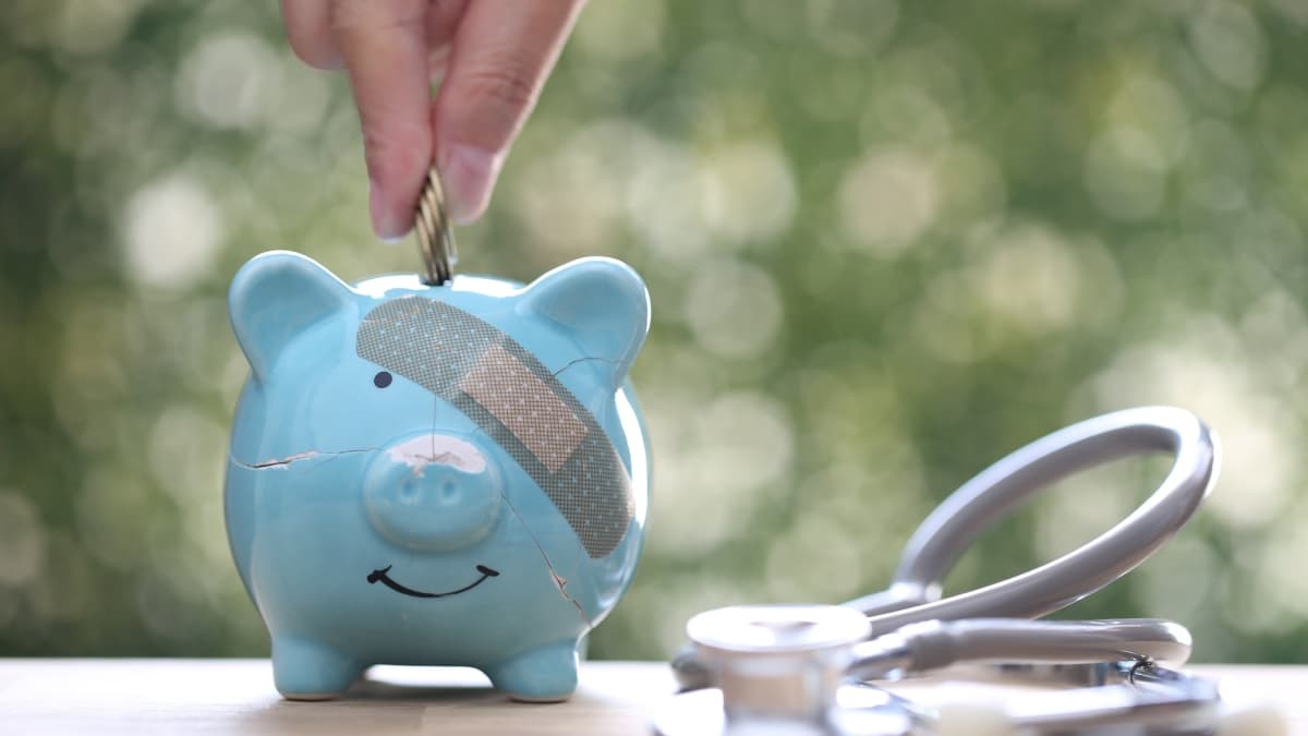 Tirelire cassée avec une main qui ajoute des pièces de monnaie dedans.
