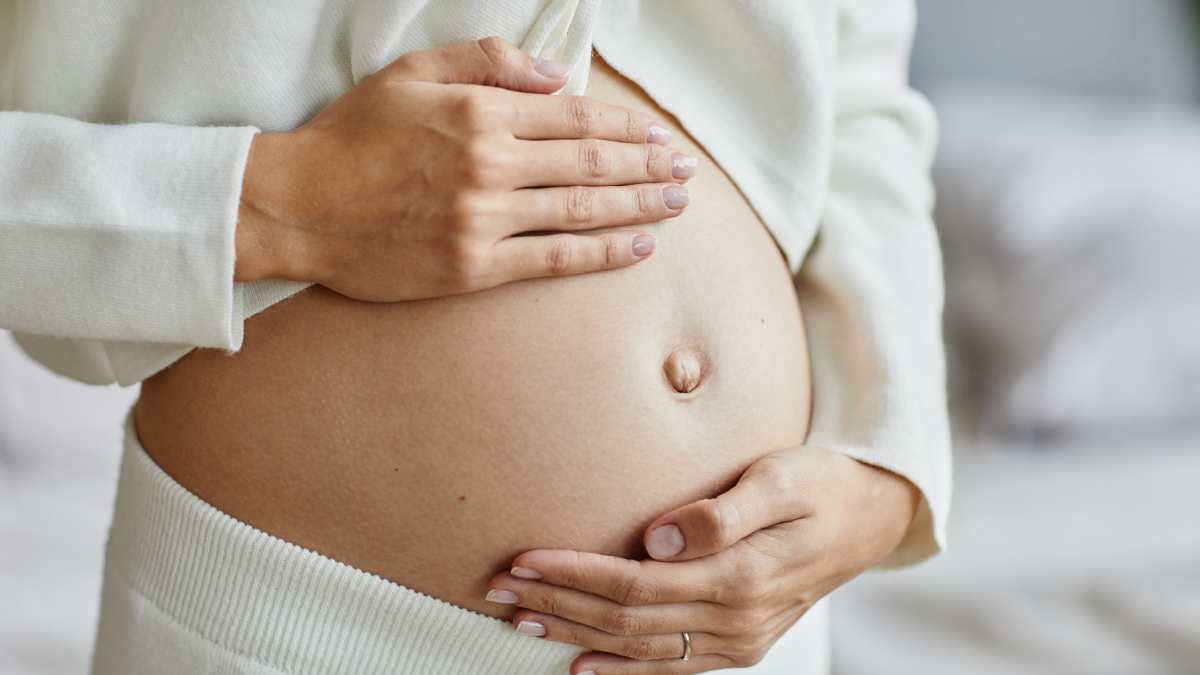 Une femme enceinte habillée en blanc qui tient son ventre.